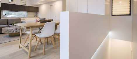 Una sala de estar moderna con un sofá, una mesa de comedor y sillas. Se observa una zona de cocina con armarios y un ventanal.