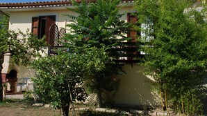 Un edificio con tejado de baldosas, puerta de madera y un pequeño jardín con árboles y arbustos.