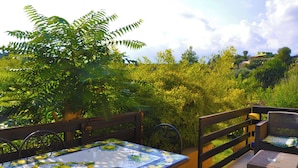 Un patio al aire libre con una mesa y sillas, rodeado de abundante vegetación y vistas a una colina.