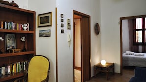 Una habitación con una estantería, una silla, una cama y una pequeña mesa con una lámpara.