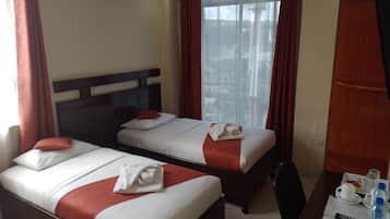 Een hotelkamer met twee bedden, een bureau met een stoel, een raam met gordijnen en uitzicht op buiten.