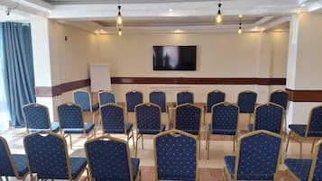 Sala de conferências com fileiras de cadeiras, um quadro branco e uma TV de tela plana na parede.