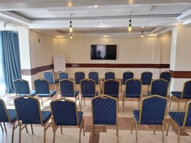 Sala de conferências com fileiras de cadeiras, um quadro branco e uma TV de tela plana na parede.