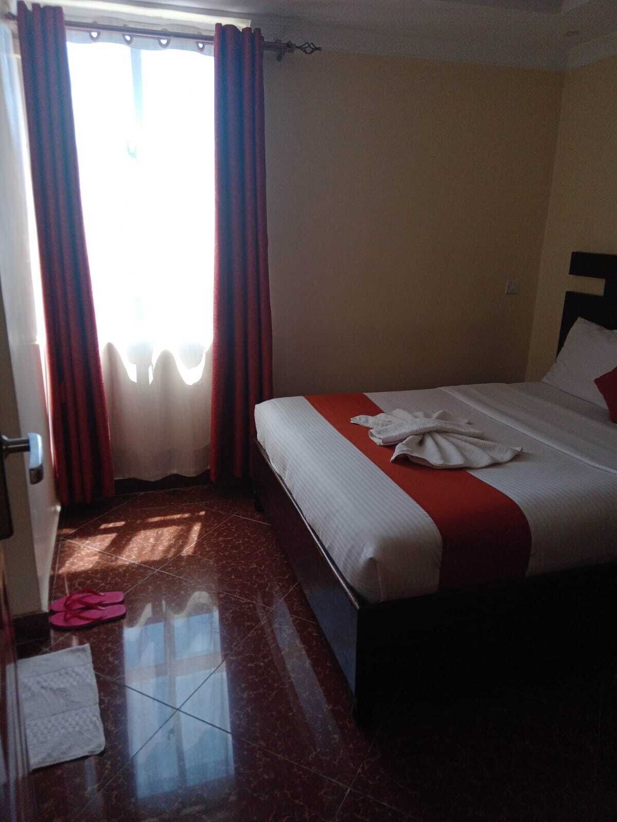 Una habitación de hotel con una cama, un ventanal con cortinas y suelo de baldosas.