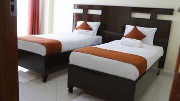 Dos camas individuales con cabeceros de madera, ropa de cama blanca y almohadas naranjas.