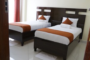 Dos camas individuales con cabeceros de madera, ropa de cama blanca y almohadas naranjas.