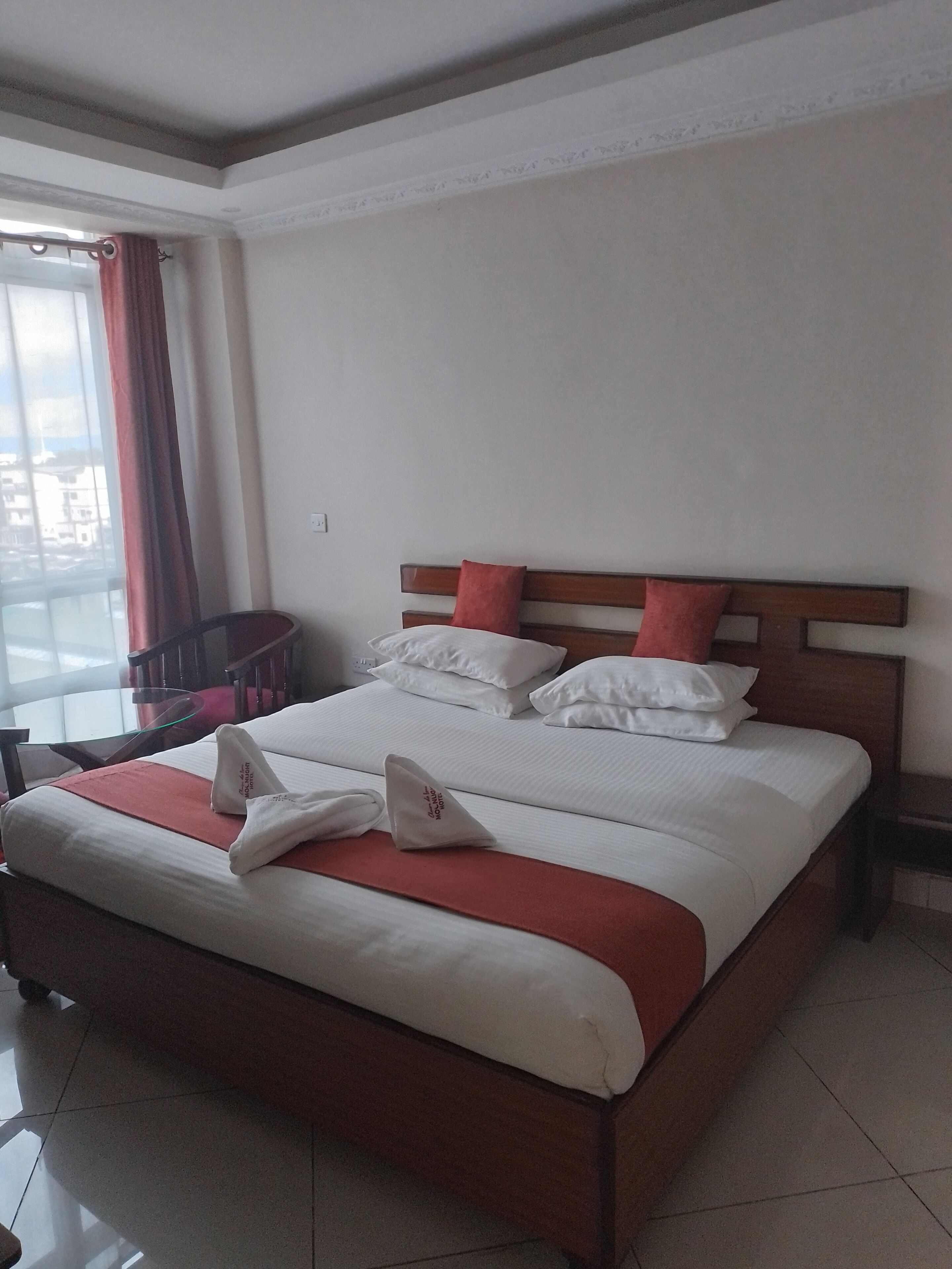 A hotel room with a large bed, a wooden headboard, and a view of the city through the window.