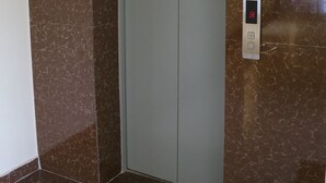 Un ascensor con pantalla digital que muestra el número 8, rodeado de paredes de mármol marrón y un suelo blanco.