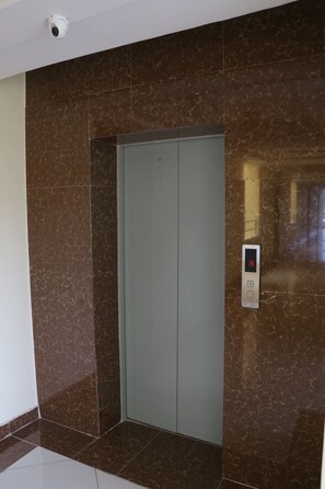 An elevator with a digital display showing the number 8, surrounded by brown marble walls and a white floor. - Claire De Lune Moonlight Hotel (Nakuru)