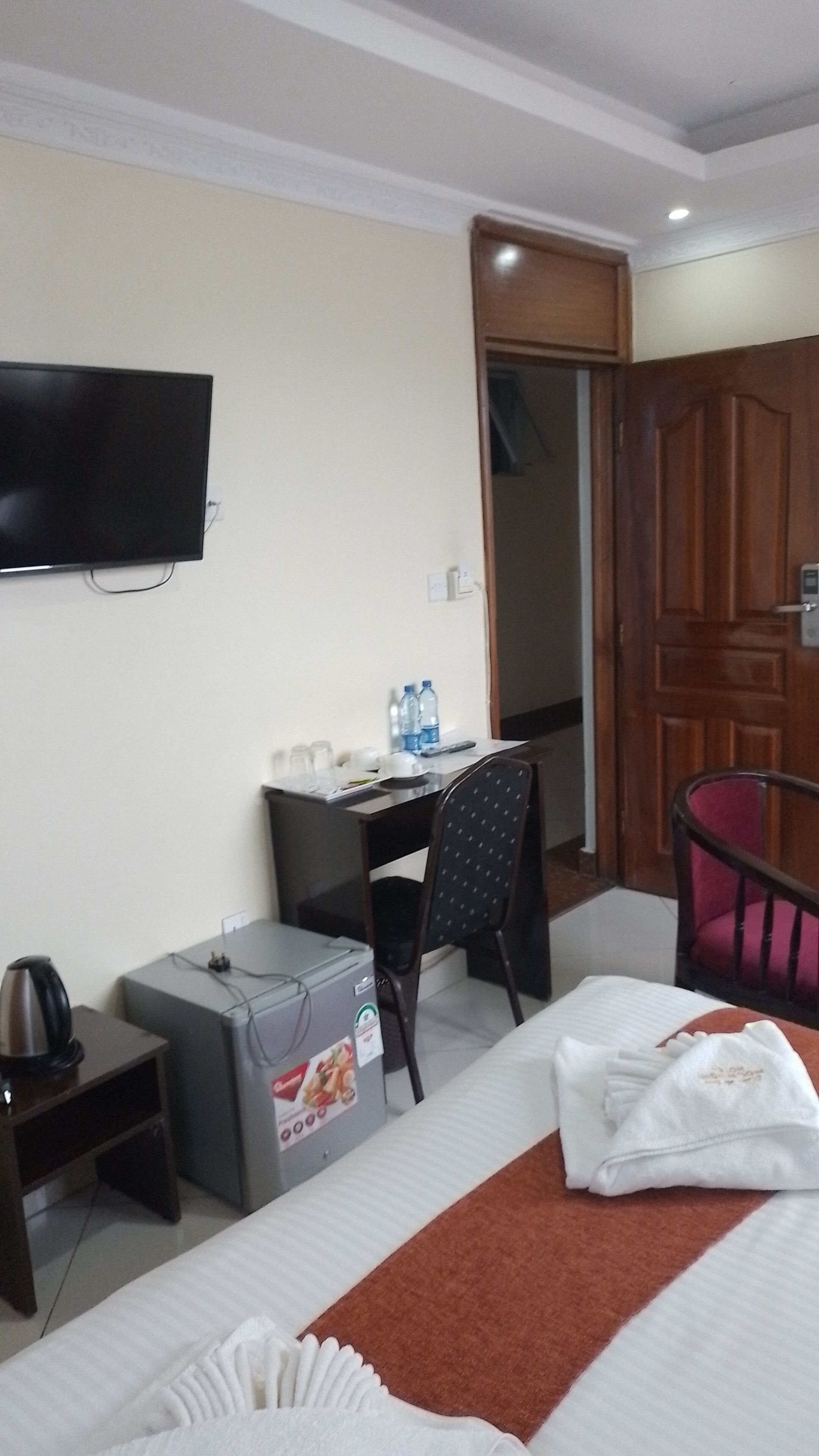 A hotel room with a bed, a desk, a chair, a television, and a minibar.