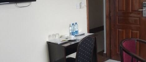 A hotel room with a bed, a desk, a chair, a television, and a minibar.