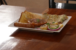 A plate with toast, a slice of omelette, a bowl of beans, and sliced onions and peppers on a wooden table.