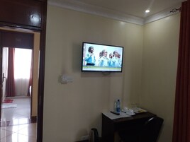 Habitación de hotel con una televisión montada en la pared, un escritorio con un control remoto, una botella de agua y una taza.