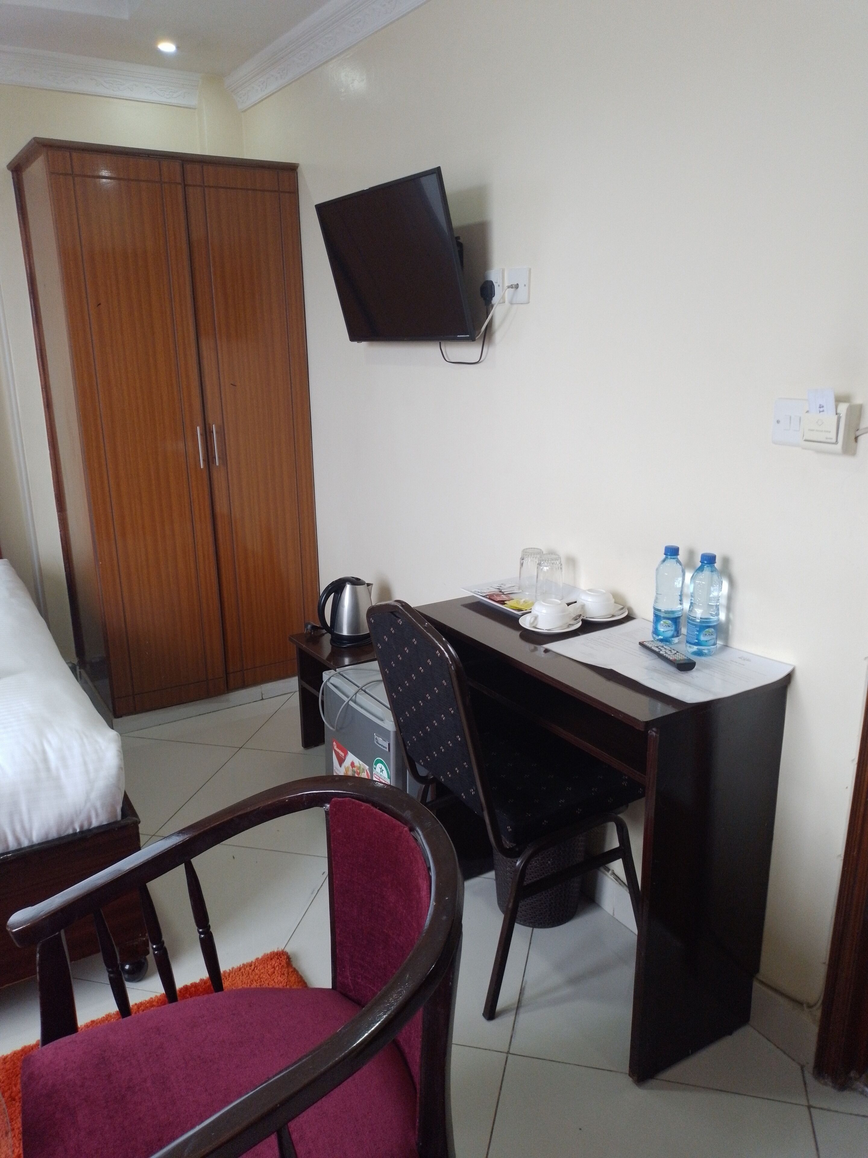 A hotel room with a bed, a desk with a chair, a television, and a wardrobe.