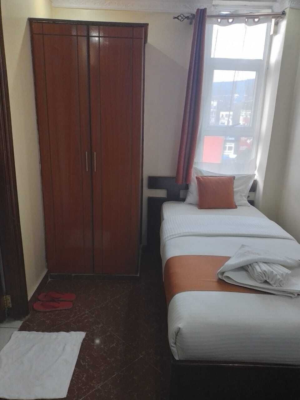 A bedroom with a bed, a wardrobe, a window with curtains, and a pair of slippers on the floor.
