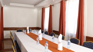 Un salón de conferencias con una mesa larga, sillas, botellas de agua y toallas.