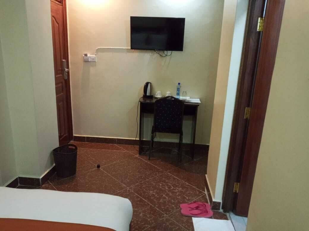 A hotel room with a bed, a desk with a chair, a television mounted on the wall, and a trash bin.