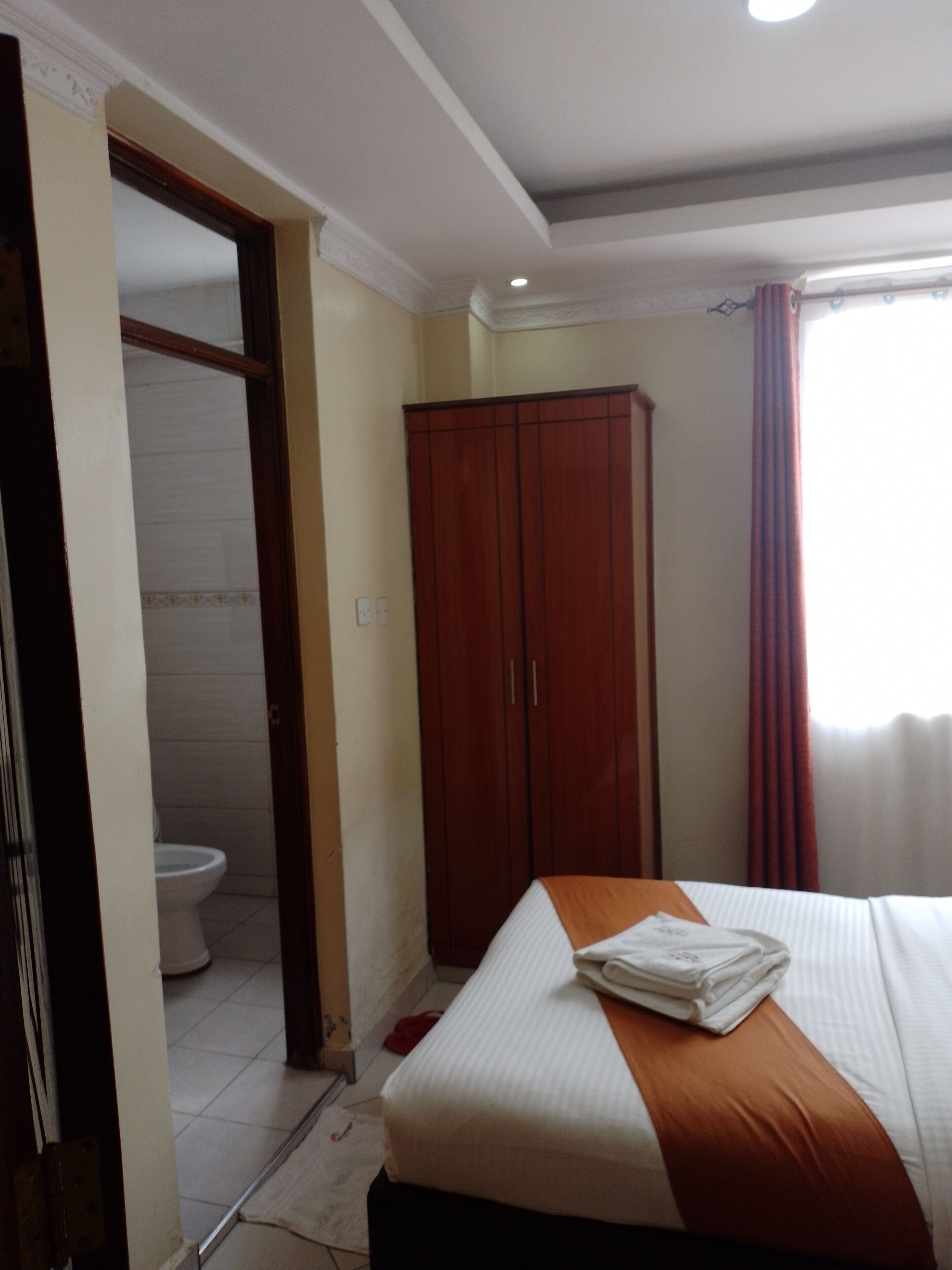 A hotel room with a bed, a wardrobe, and a bathroom visible through an open door.