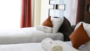 Una habitación de hotel con dos camas, cada una con ropa blanca y almohadas marrones.