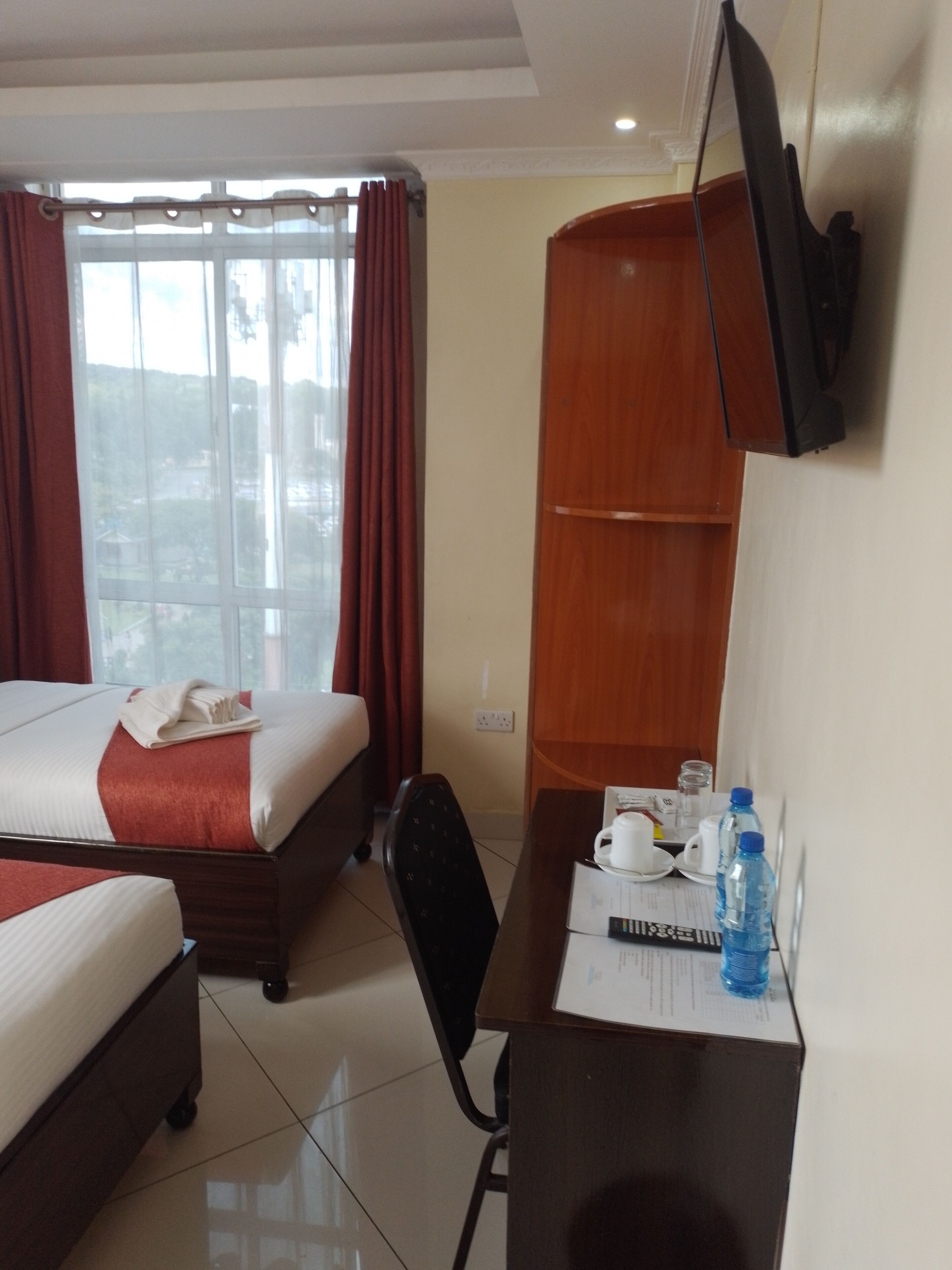 A hotel room with a bed, a desk with a chair, a television, and a window with curtains.