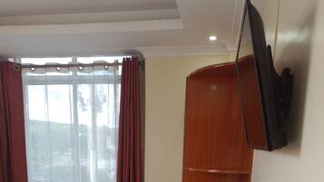 A hotel room with a bed, a desk with a chair, a television, and a window with curtains.