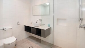 Et moderne badeværelse med toilet, vask med spejl over og en bruseniche.