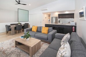Un salon moderne avec un canapé gris, une table basse en bois et un coin repas comprenant une table et des chaises blanches.
