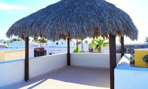 A thatched-roof structure on a rooftop with a clear view of the surrounding buildings and palm trees.