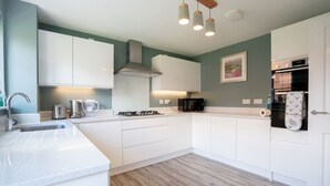 A modern kitchen with white cabinets, a gas stove, a microwave, and a sink. - Lovely 5-bed House in Centre of Bicester Village (Bicester)