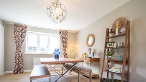 A modern living room with a wooden dining table, a bench, a bookshelf, and a geometric pendant light. - Lovely 5-bed House in Centre of Bicester Village (Bicester)