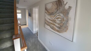 A hallway with a staircase, a large abstract painting on the wall, and a door at the end. - Lovely 5-bed House in Centre of Bicester Village (Bicester)