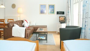A well-lit, modern hotel room with a sofa, a small table, a television, and a bed.