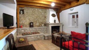 Un salón acogedor con chimenea de piedra, vigas de madera, un televisor y un sofá rojo.