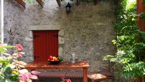 Un muro de piedra con una puerta roja, una mesa de madera con fruteros y un banco.