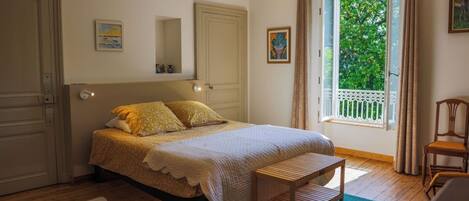 A bedroom with a bed, a wooden bench, a chair, a window with curtains, and a door.