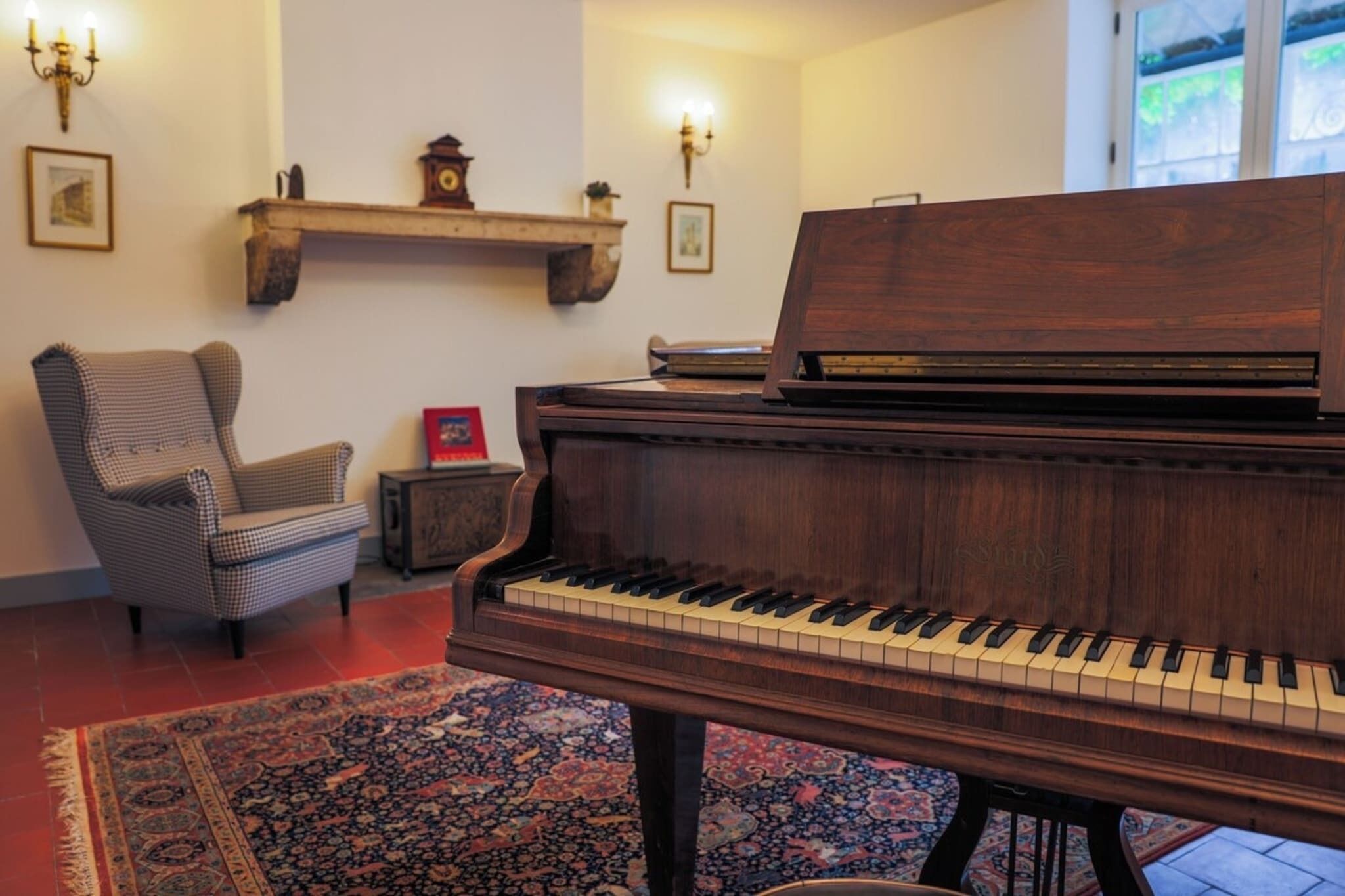 A grand piano in a room with a patterned rug, a chair, and wall-mounted shelves with decorative items.