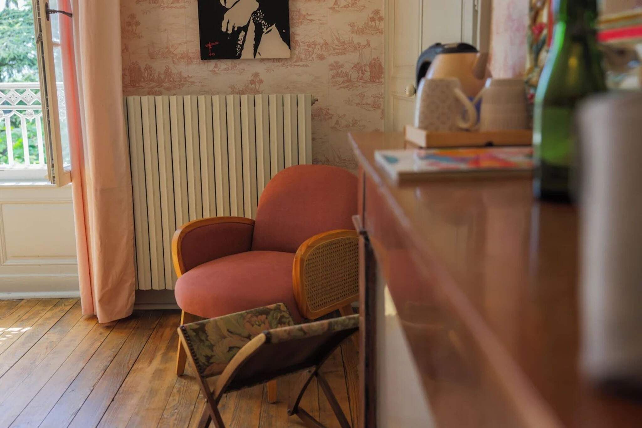 A room with a wooden floor, a red armchair, a radiator, and a window with curtains.