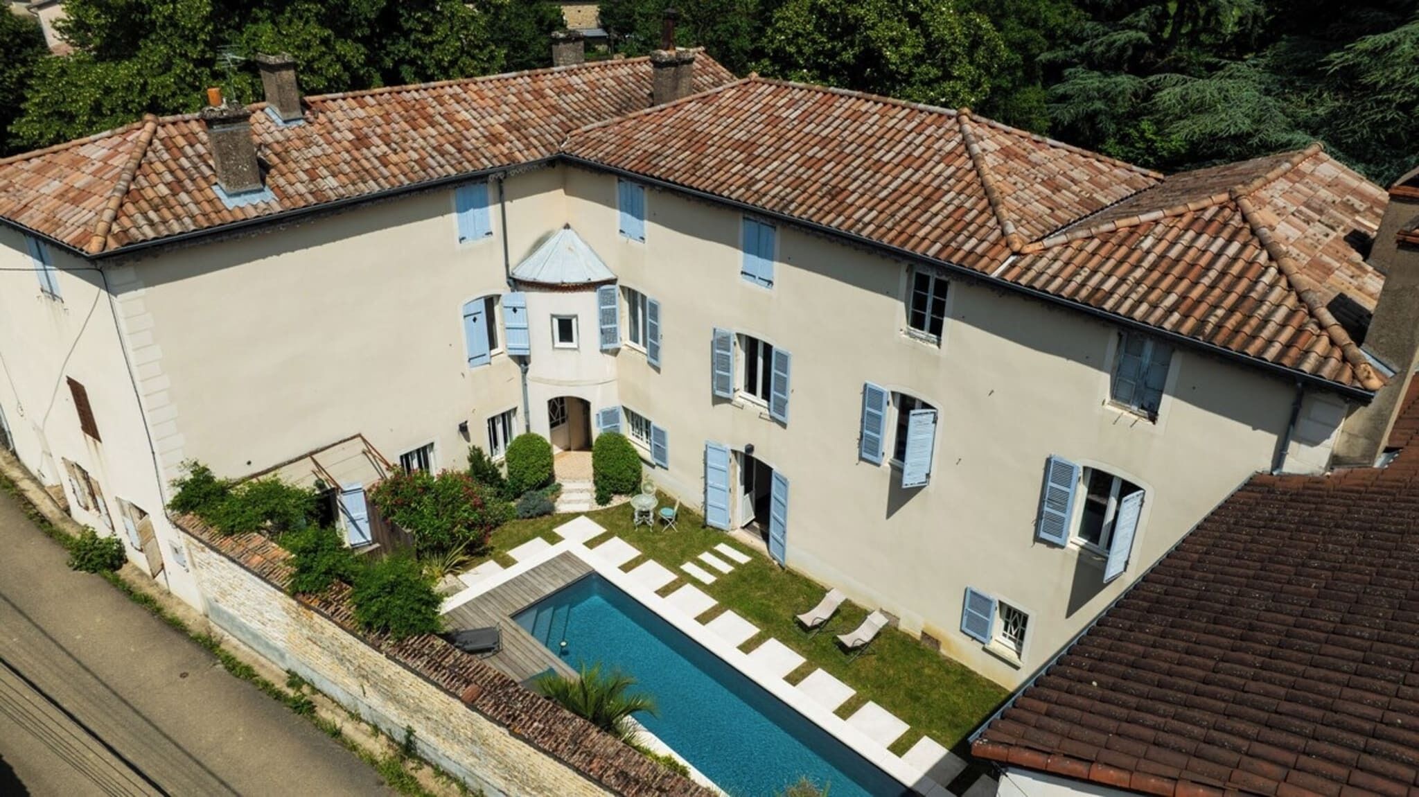 Un grand bâtiment à deux étages doté d’une piscine, de nombreuses fenêtres équipées de volets et d’une cour intérieure.
