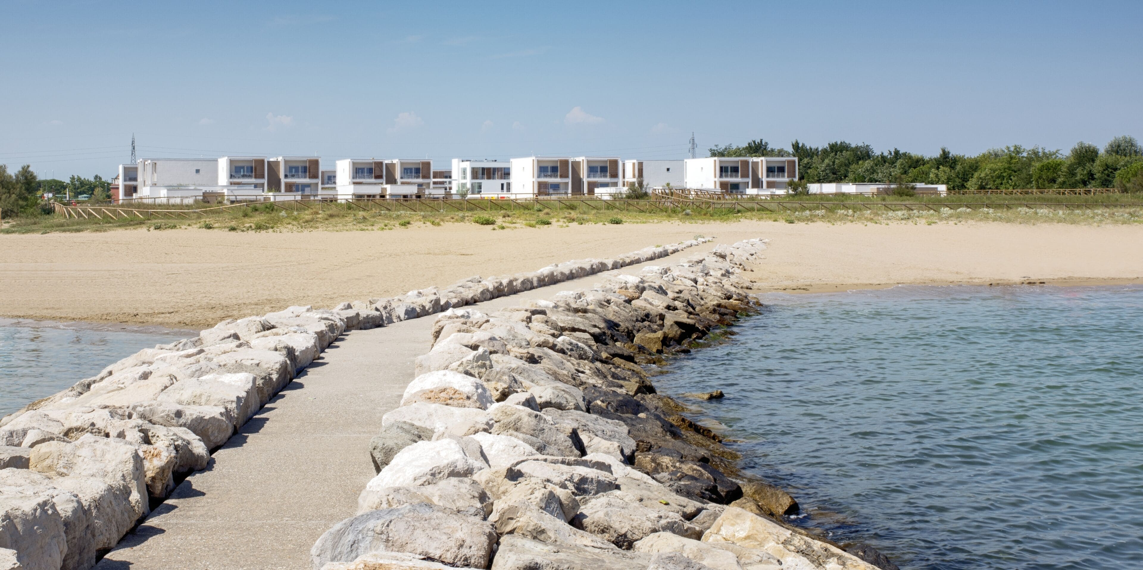 A coastal hotel with a sandy beach and a rocky breakwater.