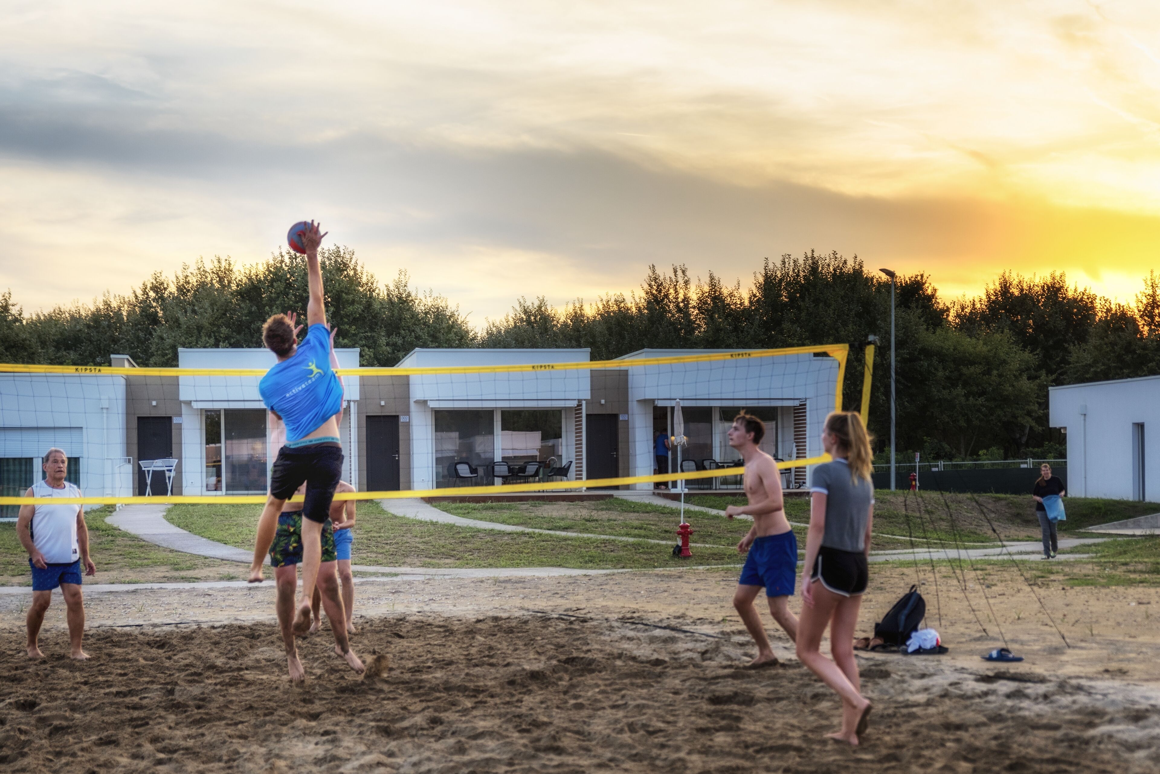 A volleyball game in progress on a sandy court with a building in the background.