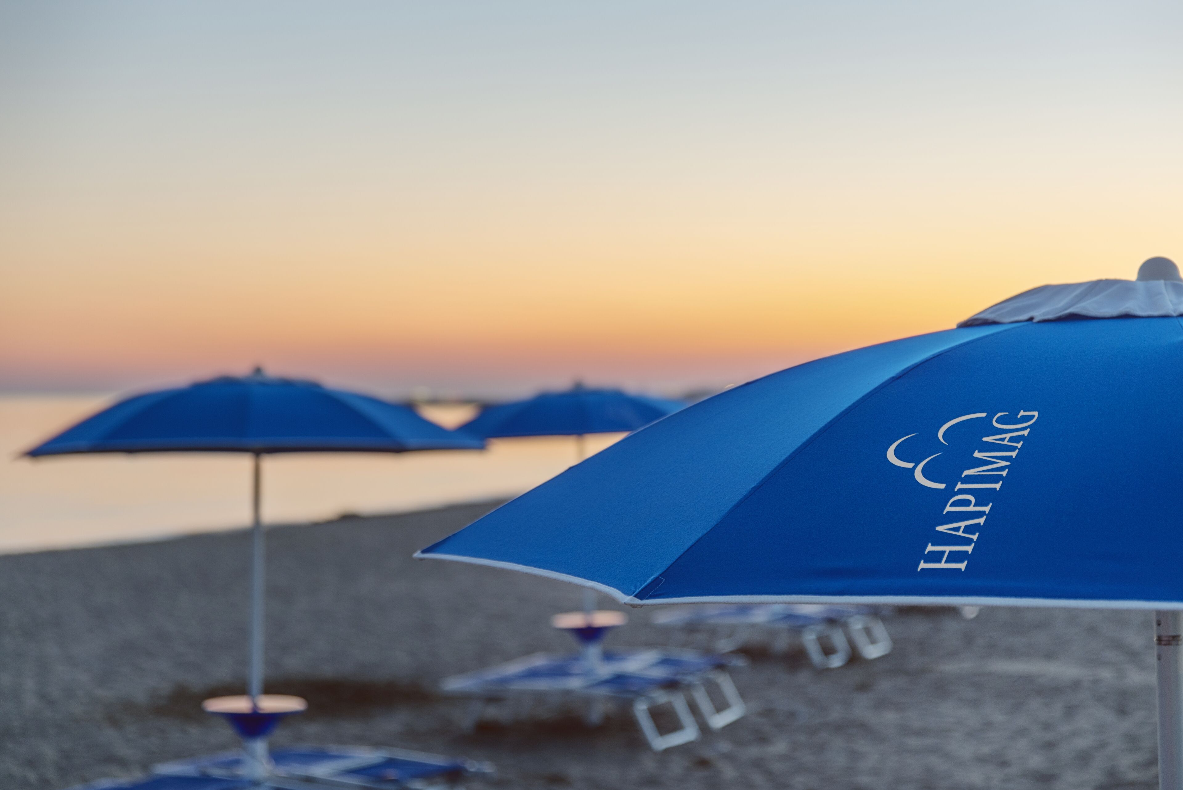 A beach scene with blue umbrellas labeled "HAPIMAG" and a clear sky.