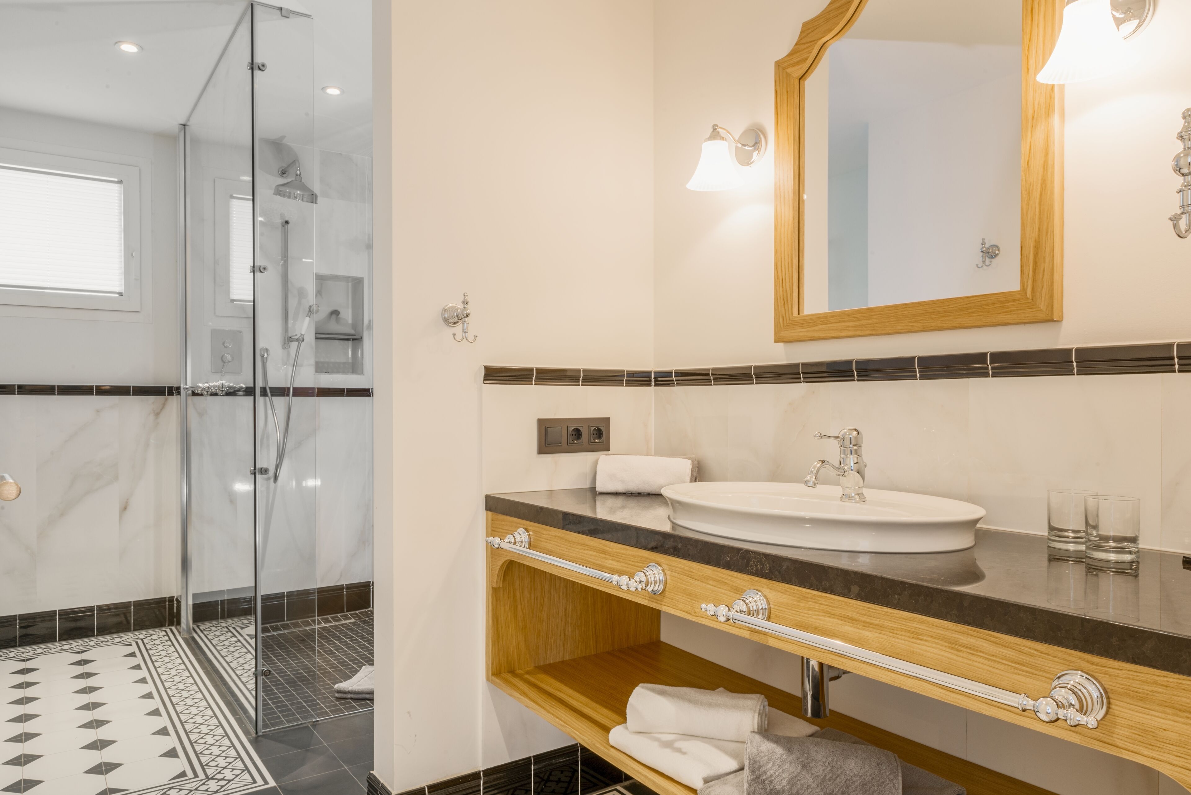 A modern bathroom with a glass-enclosed shower, a marble-tiled floor, a wooden vanity with a sink, and a large mirror.