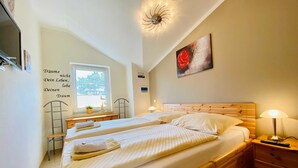 A bedroom with two beds, a window, a ceiling light, a painting, and a bedside table with a lamp.