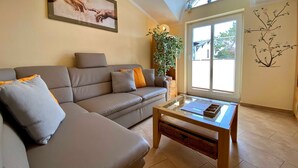 A living room with a sofa, a coffee table, a large window, and a wall-mounted plant.