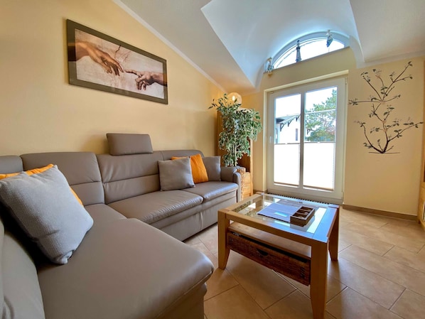 Ein Wohnzimmer mit einer Couch, einem Couchtisch, einem großen Fenster und einer Wandpflanze.