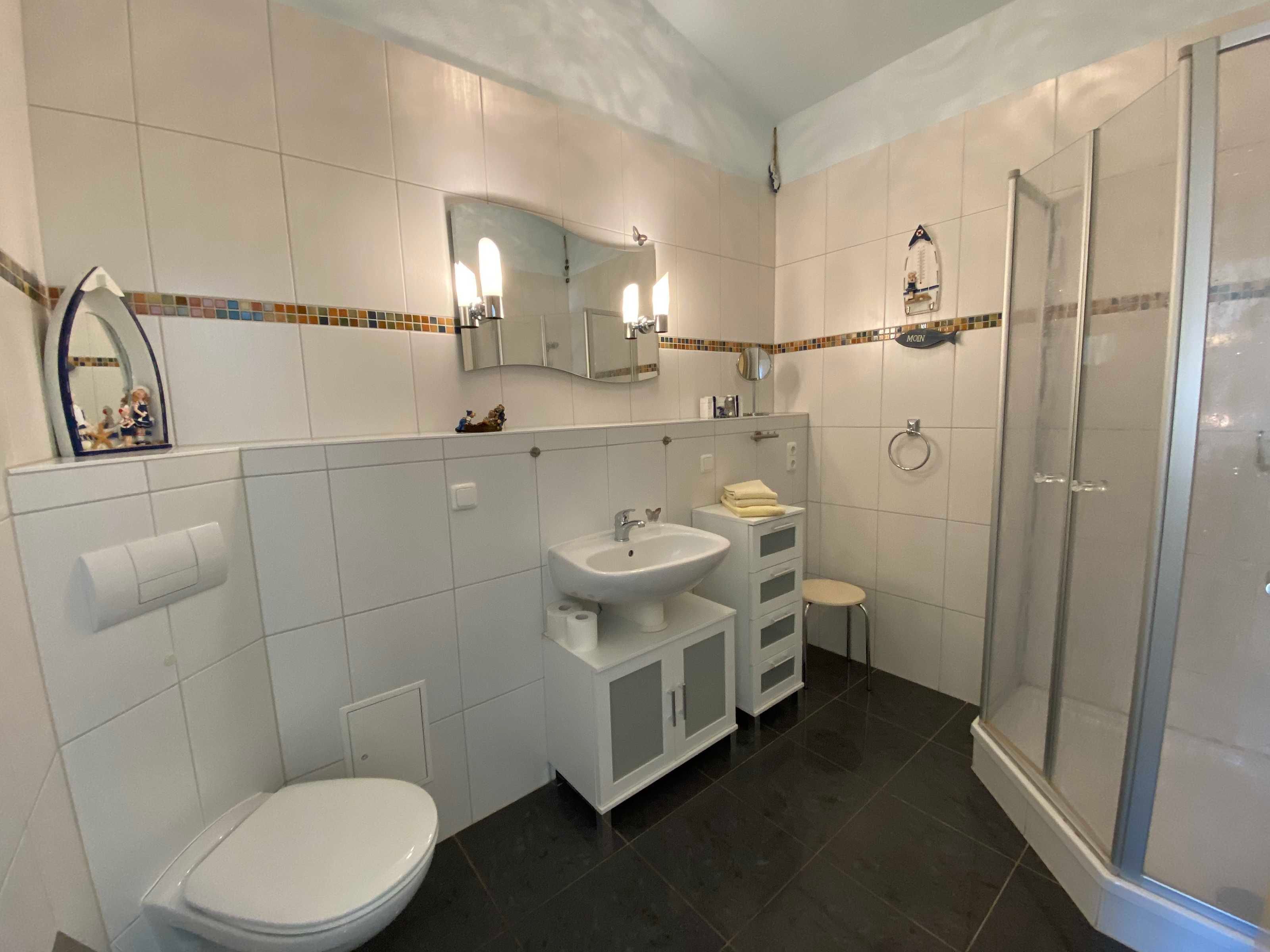 Een moderne badkamer met toilet, wastafel, badkamermeubel en douche.
