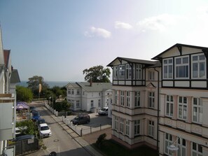 Un barrio residencial con varias casas de dos pisos, una calle con coches aparcados y vista al mar de fondo.