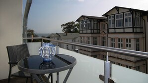 A balcony with a round table and a blue vase, overlooking a row of houses with a clear sky.