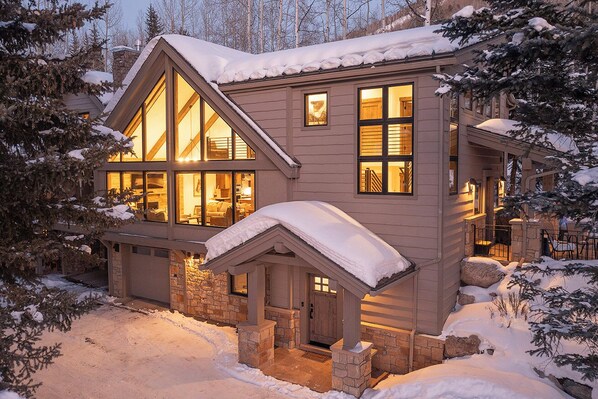 A two-story house with large windows, a stone foundation, and a snow-covered roof. - GreenHill Court Chalet | 5BR Luxury Vail Chalet, Summer AC (Vail)