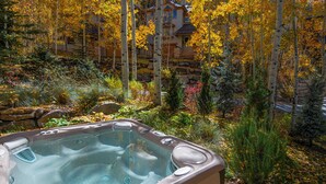 Un bain à remous entouré de feuillages d’automne et bordé d’un mur de pierres.